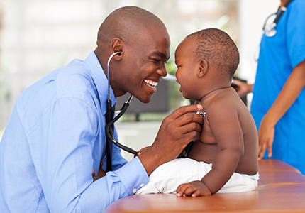 A young African-American doctor smiles while listening to the heartbeat of an African-American baby.